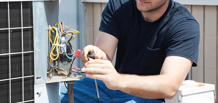 A technician is inspecting the wires of an outdoor air conditioning unit.