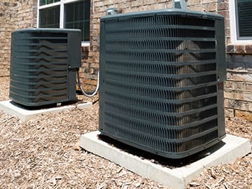 Two large outdoor air conditioning units on cement platforms.