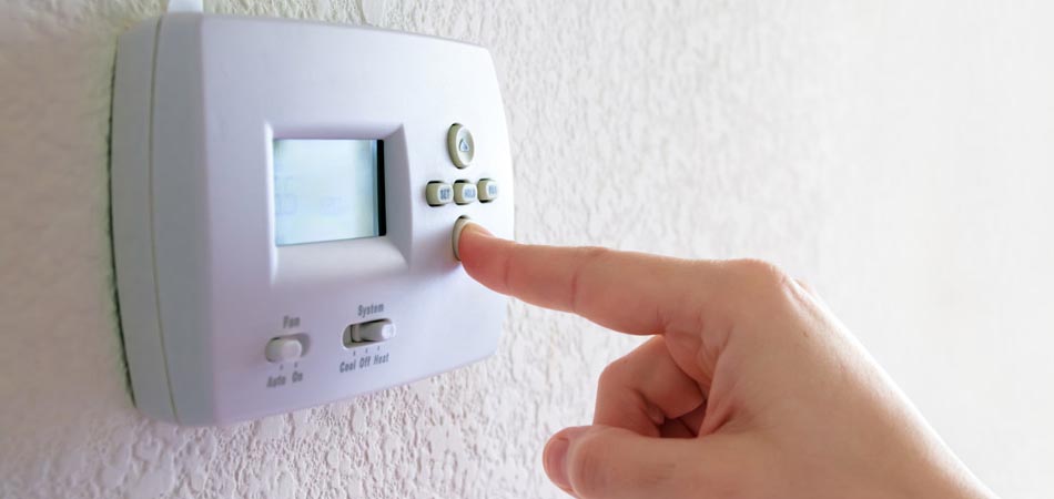 A person adjusting their thermostat to reduce the temperature.