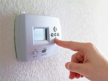 A person is pushing a button on a thermostat to adjust the heating level.